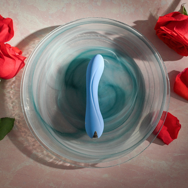 Evolved Blue Crush: light blue curved silicone bullet vibrator in a glass dish, surrounded by red roses