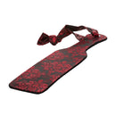 Scandal Paddle lying flat at an angle, showing the brocade side and the tied handle loop